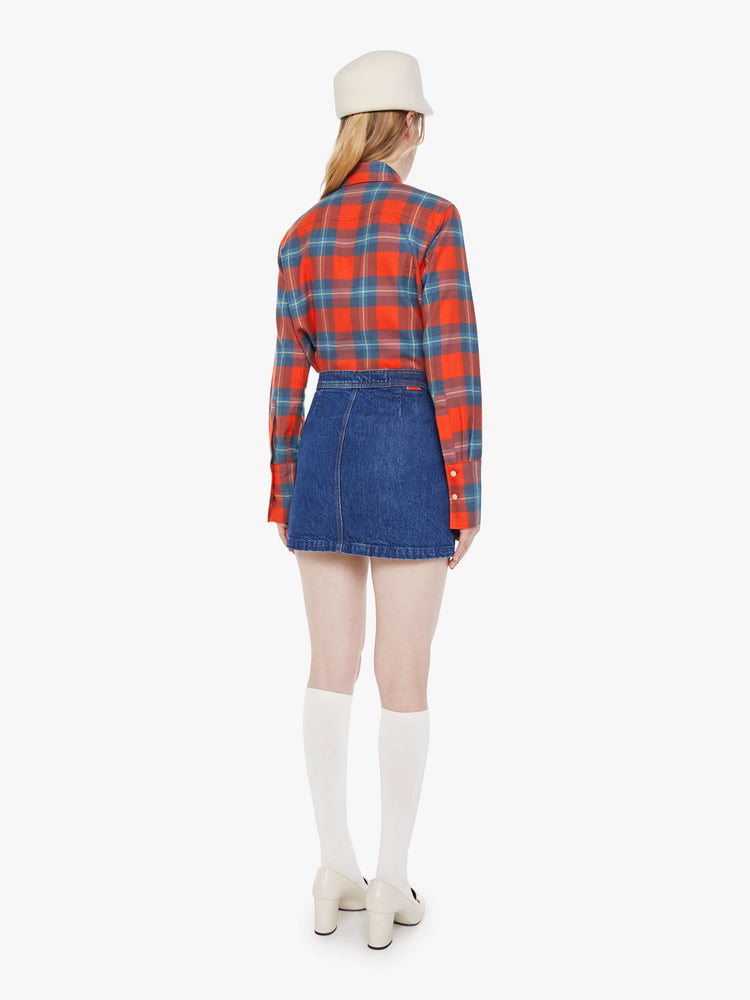 Back view of a woman in a mid blue denim mini skirt with a high rise, button fly, small pockets at the waist and a short hem.