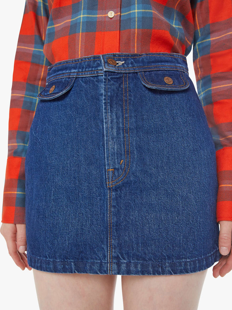 Close up view of a woman in a mid blue denim mini skirt with a high rise, button fly, small pockets at the waist and a short hem.
