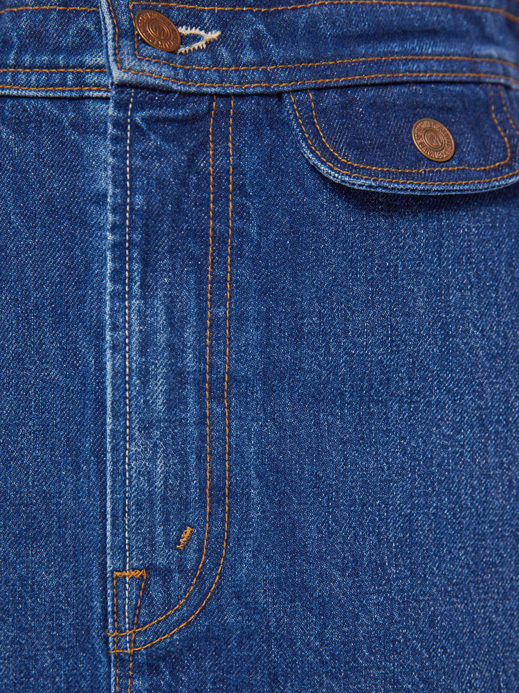 Close up view of a woman in a mid blue denim mini skirt with a high rise, button fly, small pockets at the waist and a short hem.