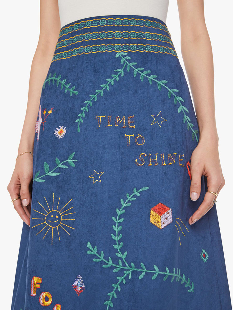 Close up view of a woman in an A-line skirt with a high rise, side-zip closure and a calf-length hem in a deep navy with colorful embroidered leaves, text and doodles throughout.