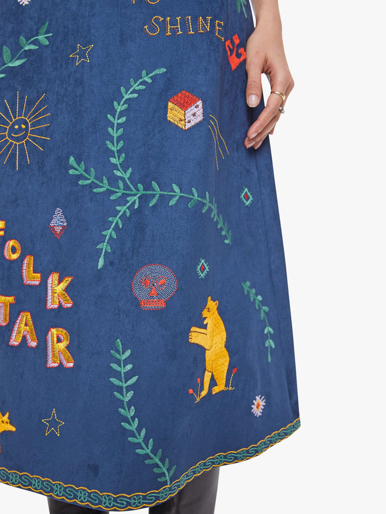 Close up view of a woman in an A-line skirt with a high rise, side-zip closure and a calf-length hem in a deep navy with colorful embroidered leaves, text and doodles throughout.