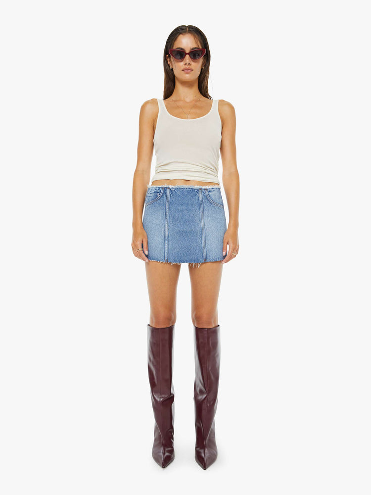 Front view of a woman in a med blue skirt has a raw hem and waistband, a back zip closure and a playfully short fit.