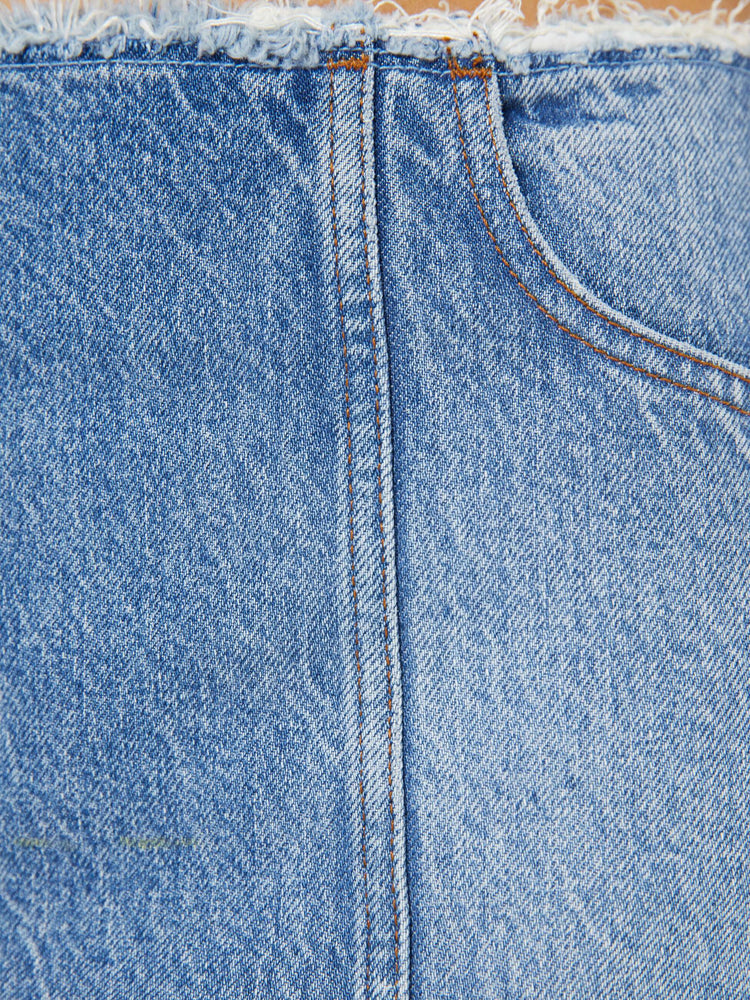 Swatch view of a woman in a med blue skirt has a raw hem and waistband, a back zip closure and a playfully short fit.