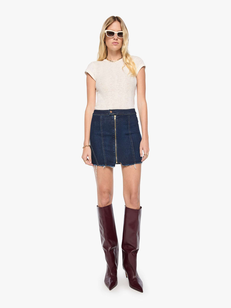 Front view of a woman in a dark denim low-slung mini skirt with a button-tab waistband, zip closure down the front and a raw, frayed hem.