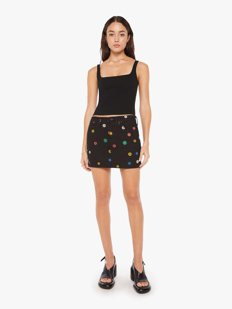 Front view of a woman in denim mini skirt with a high rise, button fly, slim fit and thigh-grazing hem in a black shade with colorful printed daisies throughout.