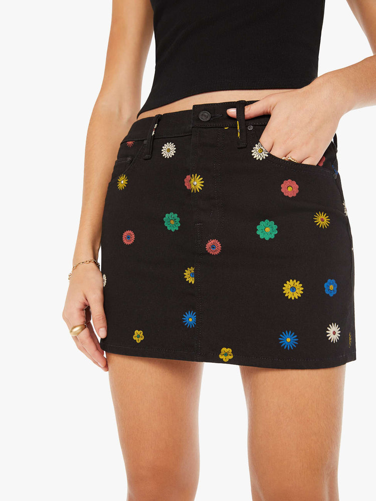 Close up view of a woman in denim mini skirt with a high rise, button fly, slim fit and thigh-grazing hem in a black shade with colorful printed daisies throughout.