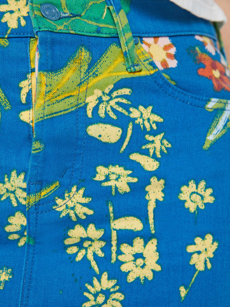 Detailed view of a woman in a bright blue mini skirt with an oversized tropical floral print, high rise, button fly, slim fit and thigh-grazing hem. 
