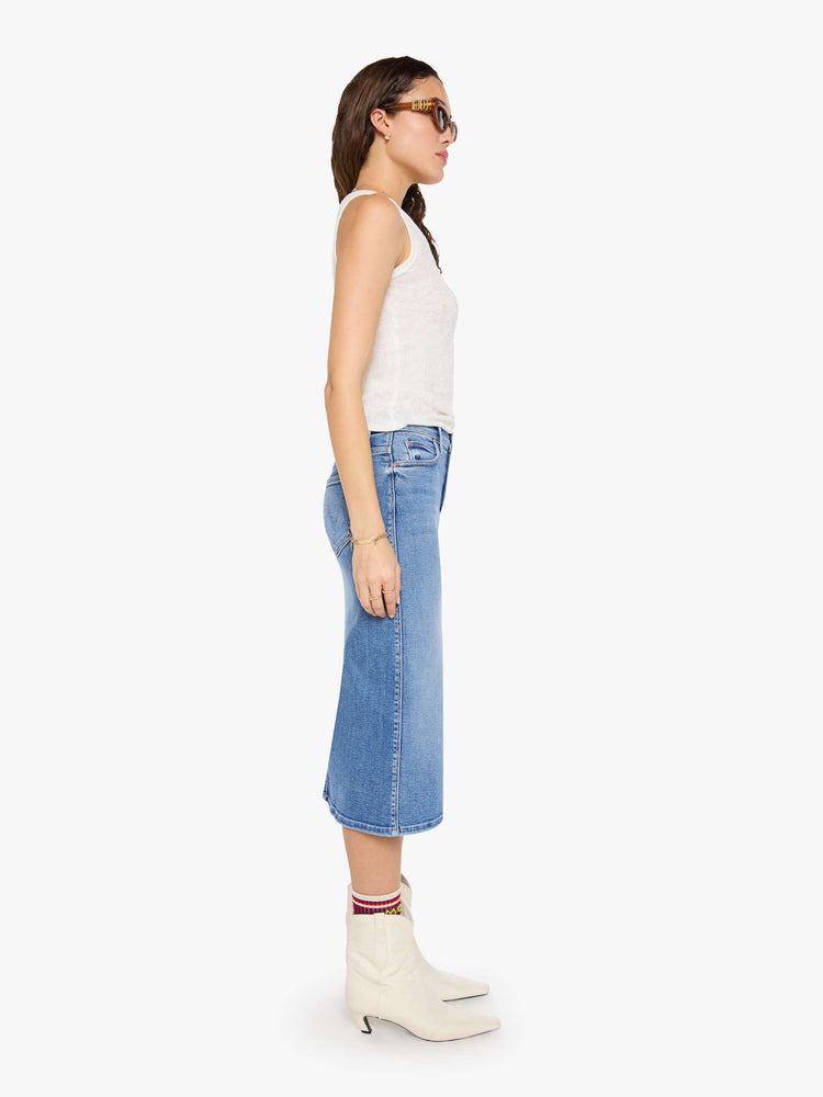 Side view of a woman in med blue denim midi skirt with a zip fly and an A-line fit.