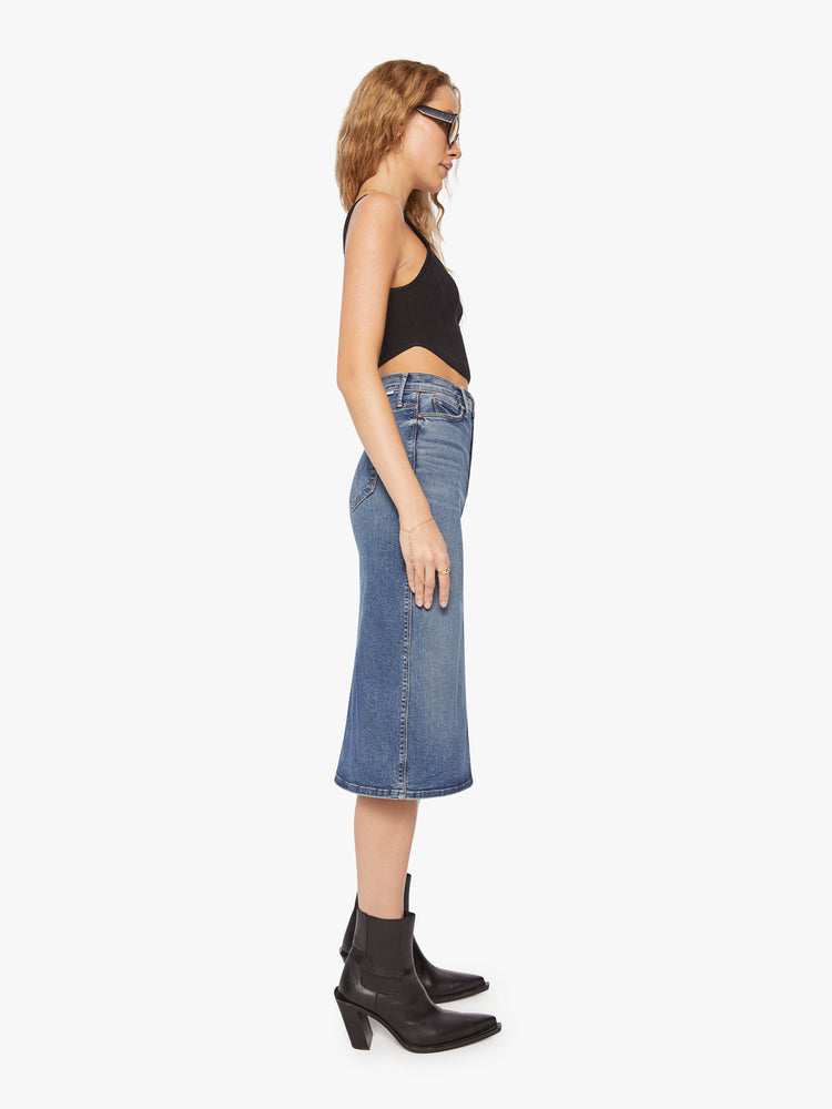 Side view of a woman high waisted denim midi skirt with an A-line fit and a clean hem that hits just below the knee in a mid-blue wash.