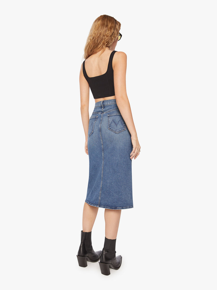 Back view of a woman high waisted denim midi skirt with an A-line fit and a clean hem that hits just below the knee in a mid-blue wash.