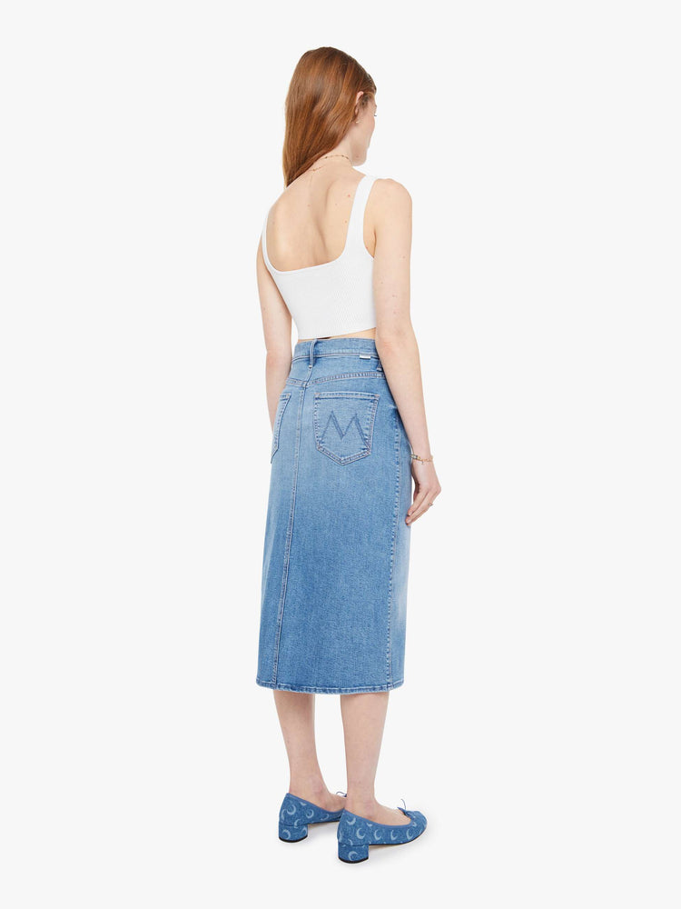 Back view of a woman in a light blue  high-waisted denim midi skirt with a zip fly, A-line fit and calf-length hem. 