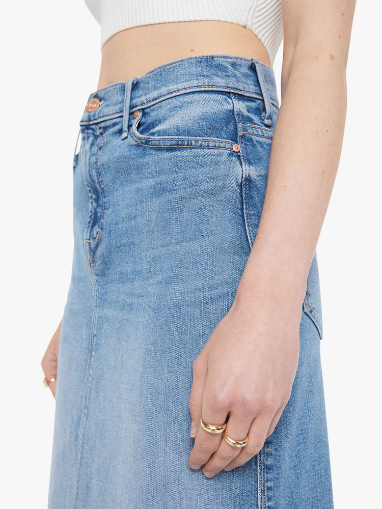 Close up waist view of a woman in a light blue  high-waisted denim midi skirt with a zip fly, A-line fit and calf-length hem. 