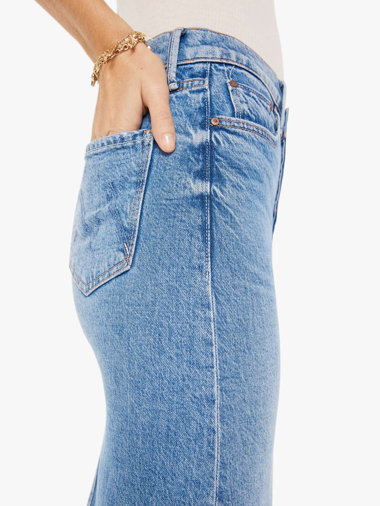 Side close up view of a woman wearing a medium blue wash denim midi skirt featuring a relaxed mid rise, paired with a white tank top.