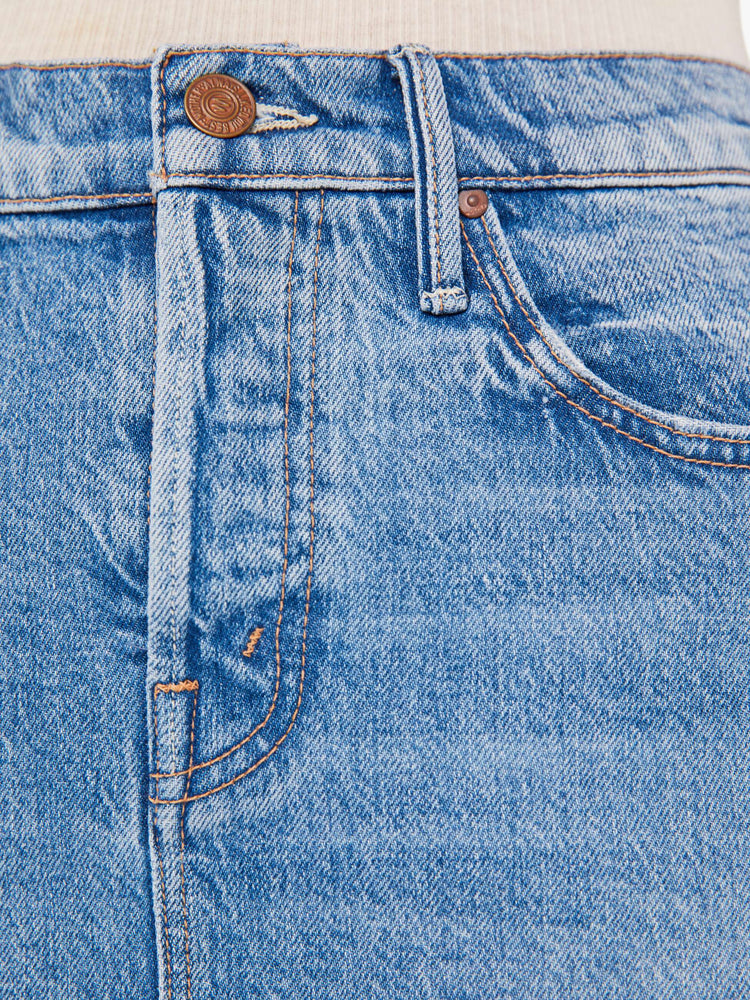 A close up swatch detail view of a medium blue wash jean featuring copper hardware and contrast brown stitching.