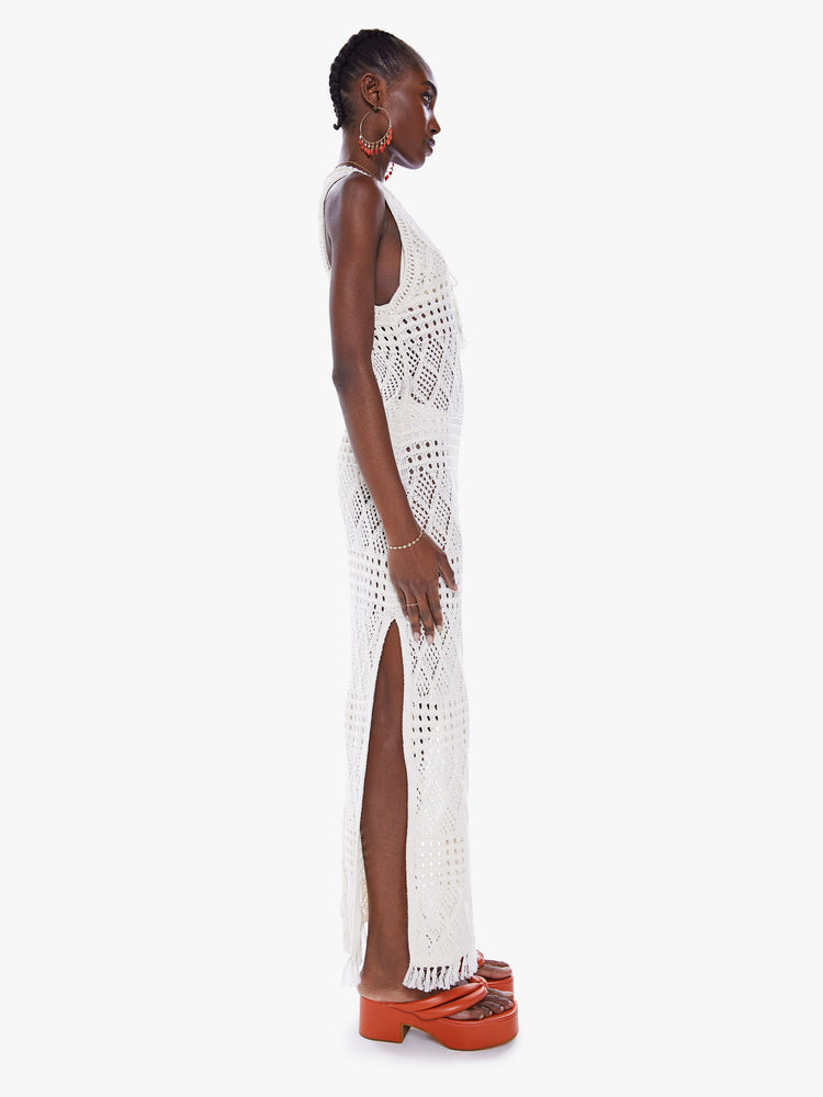 Side view of a woman maxi dress with thigh-high side slits and a slim fit in a sheer crochet fabric with fringe at hem.