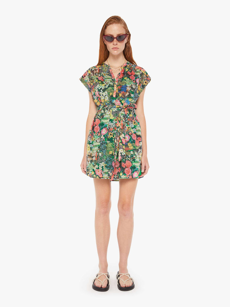 A front full body view of a woman wearing a short sleeve shirt dress, featuring a colorful garden print and a waist tie.