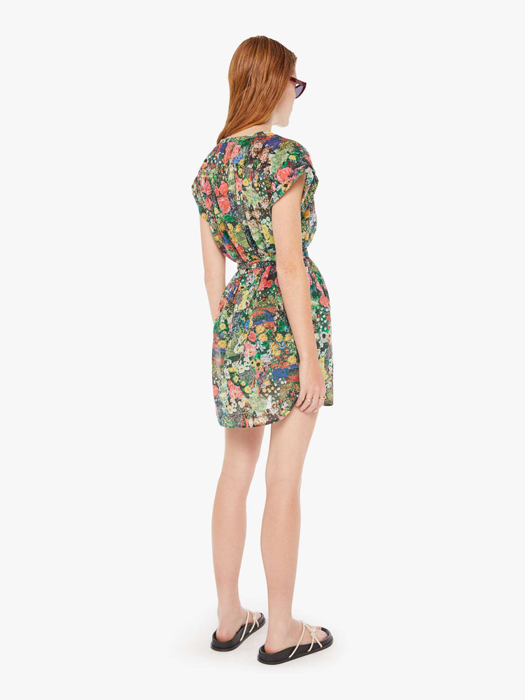 A back full body view of a woman wearing a short sleeve shirt dress, featuring a colorful garden print and a waist tie.