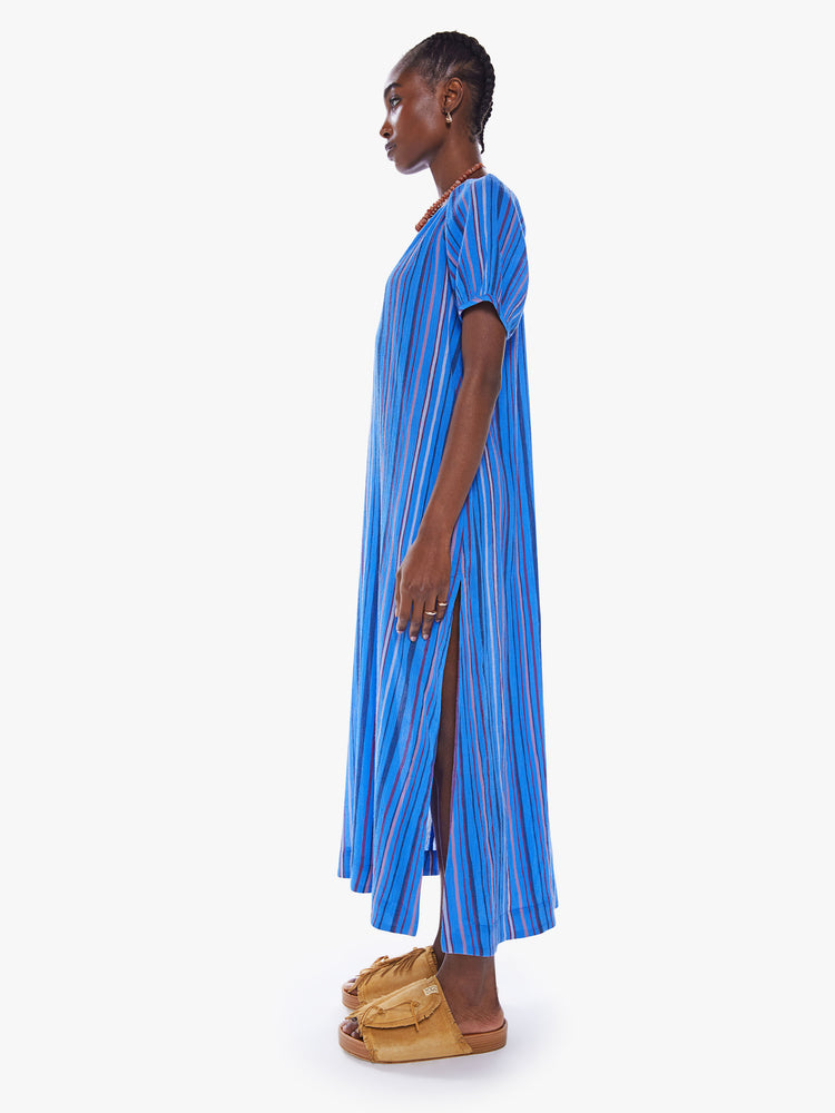 Side view of a woman maxi dress with a V-neck, short puffed sleeves, side slits in a blue stripe pattern.