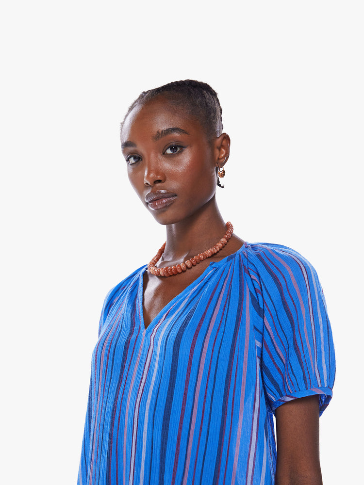 Close up view of a woman maxi dress with a V-neck, short puffed sleeves, side slits in a blue stripe pattern.