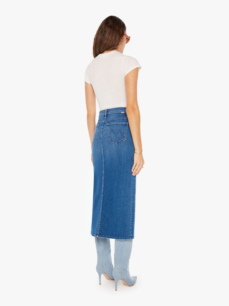 Back view of a woman denim pencil skirt with a high rise, narrow fit and a thigh-high front slit in a mid blue wash.