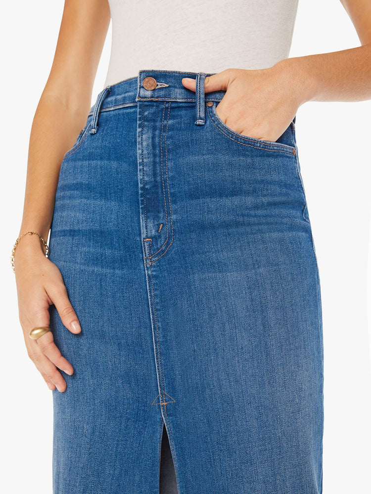 Close up view of a woman denim pencil skirt with a high rise, narrow fit and a thigh-high front slit in a mid blue wash.