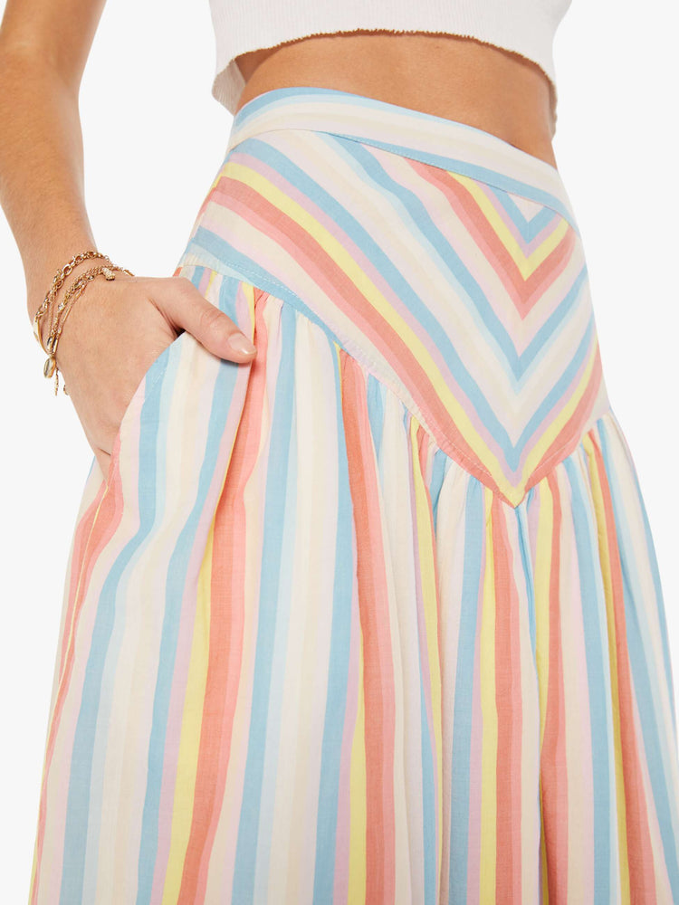 Side close up view of a woman wearing a woven skirt featuring a colorful stripe pattern, a triangle panel in the front with a ruffled full skirt and side pockets.