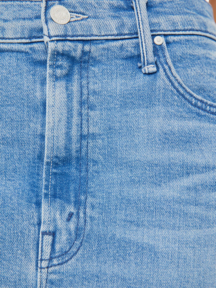 Detailed view of a woman in a light blue high-rise denim midi skirt with a diagonal thigh-high slit and a narrow fit with whiskering and fading at the knees.