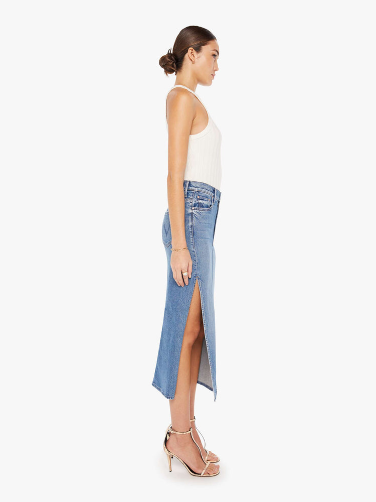 Side view of a womens medium blue wash denim skirt featuring a high rise and a high side slit.
