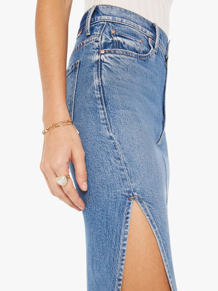 Side close up view of a womens medium blue wash denim skirt featuring a high rise and a high side slit.