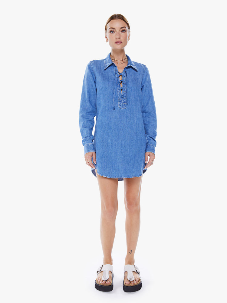Front view of a women collared shirt dress with a deep V-neck that laces and ties, long sleeves and a playfully short curved hem in a mid-blue wash.