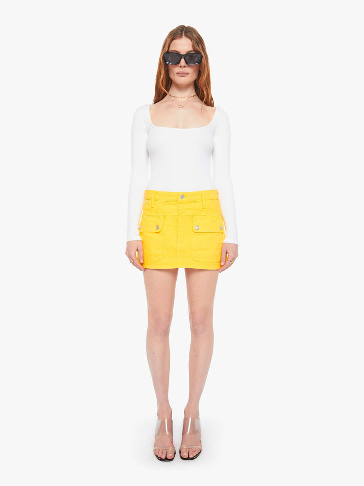 Front view of a woman in a yellow mini skirt with patch pockets, a zip fly and playfully short hem.