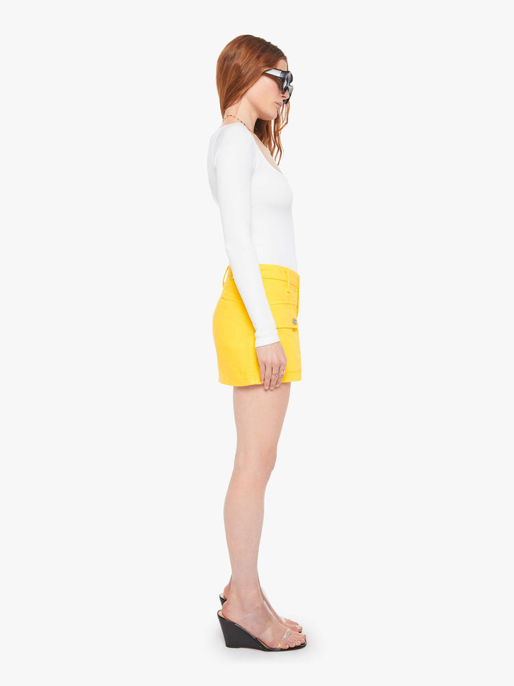 Side view of a woman in a yellow mini skirt with patch pockets, a zip fly and playfully short hem.