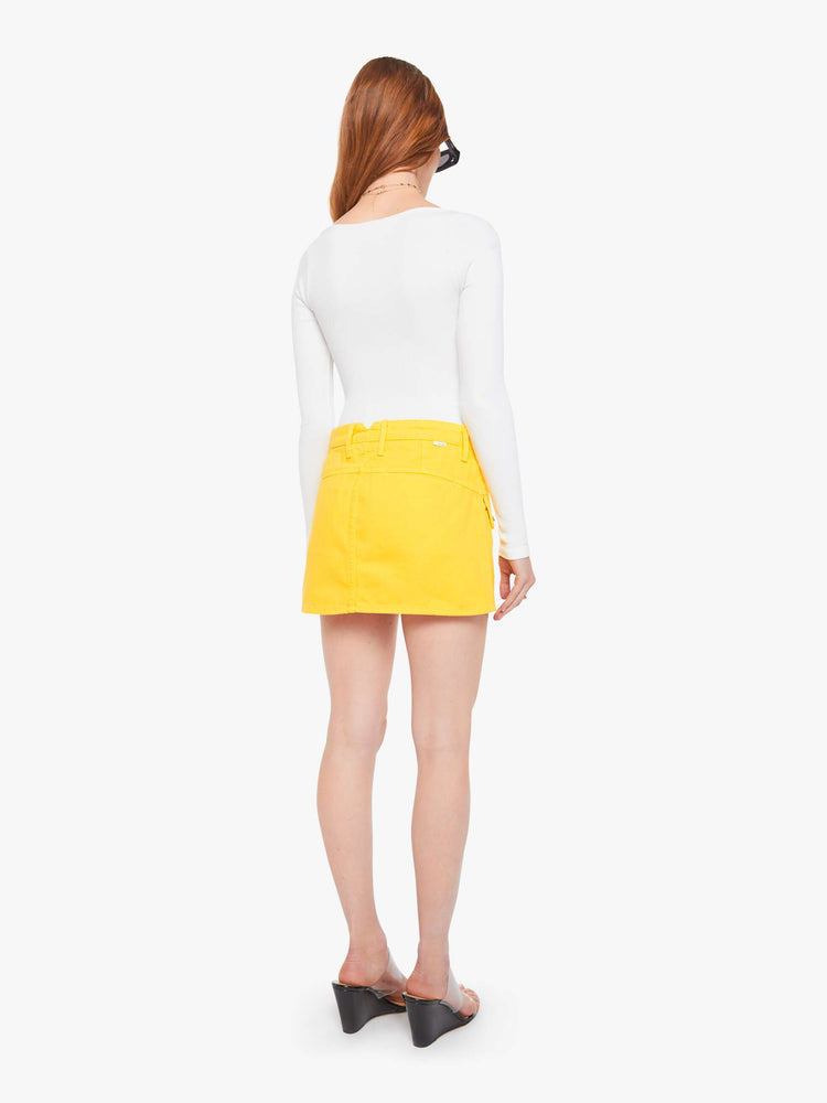 Back view of a woman in a yellow mini skirt with patch pockets, a zip fly and playfully short hem.