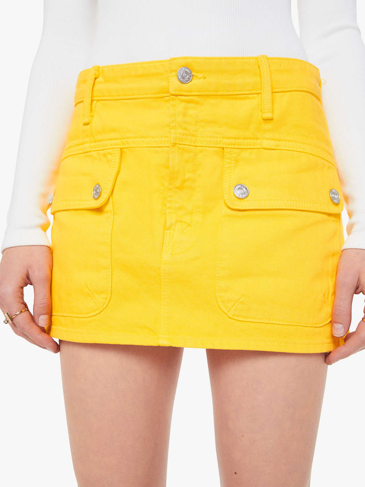 Close up view of a woman in a yellow mini skirt with patch pockets, a zip fly and playfully short hem.