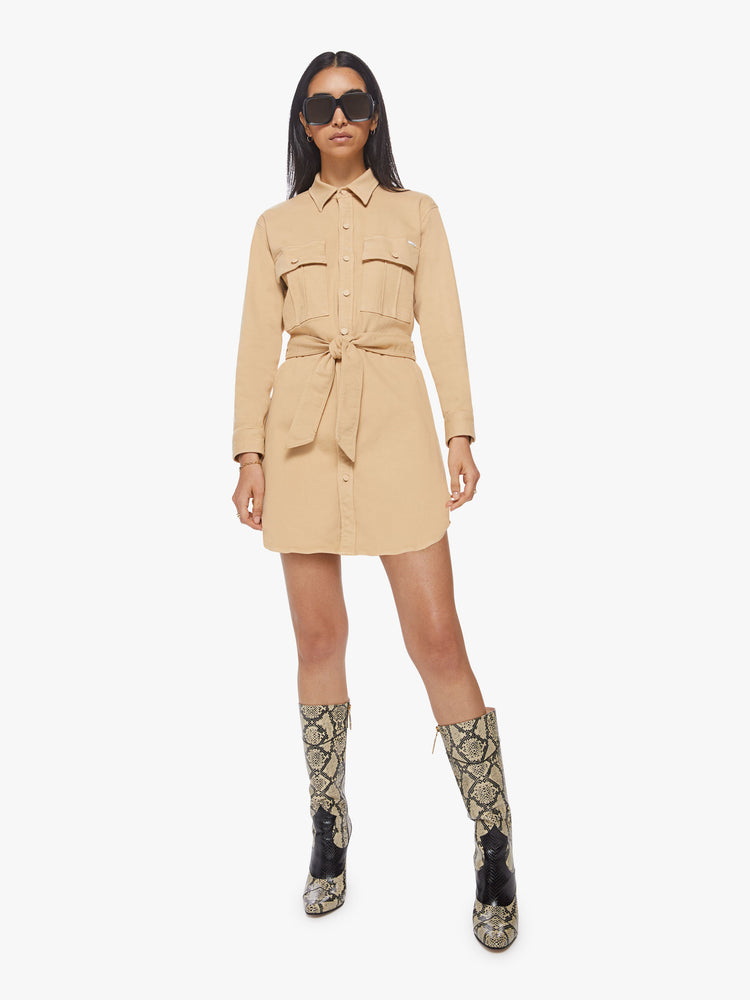 Front view of woman sandy mini shirt dress with long sleeves, a collared neck, buttons down the front and a tied belt at the waist.
