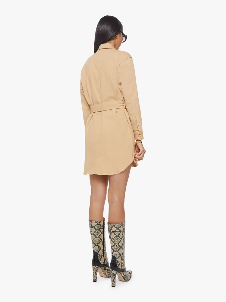 Back view of woman sandy mini shirt dress with long sleeves, a collared neck, buttons down the front and a tied belt at the waist.