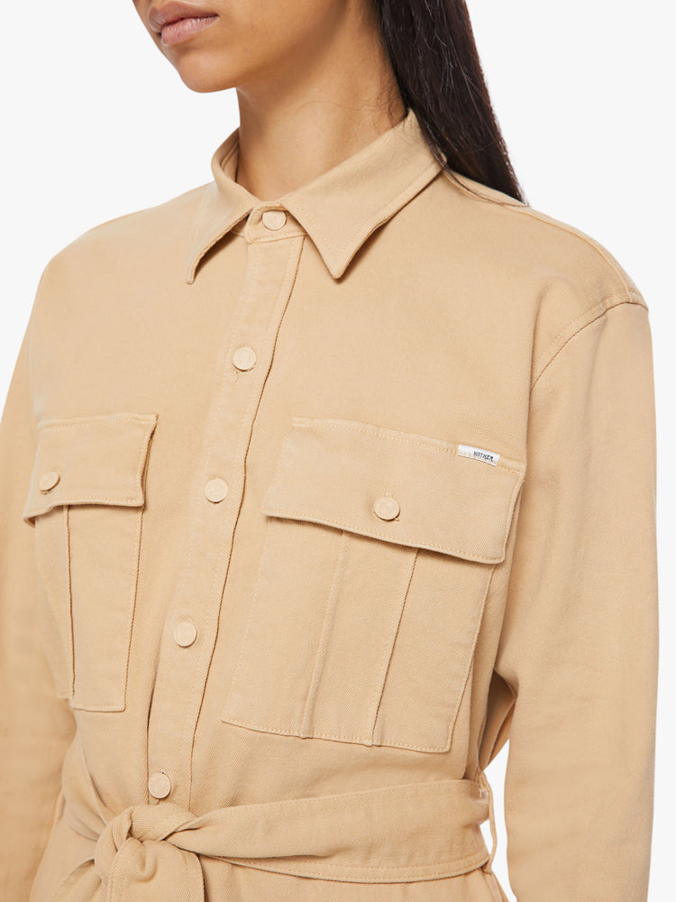 Close up view of woman sandy mini shirt dress with long sleeves, a collared neck, buttons down the front and a tied belt at the waist.