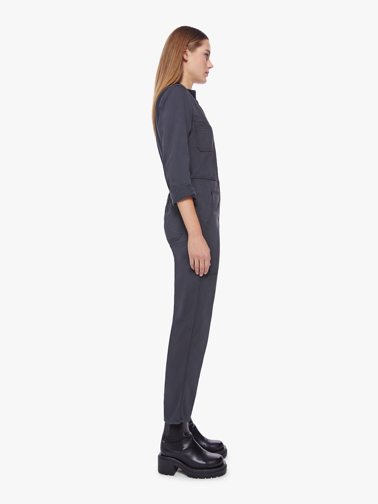 Side view of a woman faded black workwear-inspired zip-up jumpsuit with a collared neck, patch pockets, high rise elastic waistband, 3/4-sleeves and an ankle-length inseam.