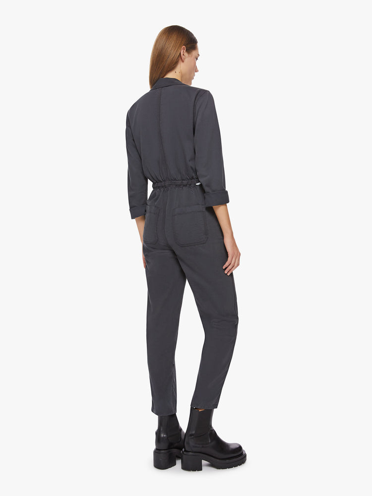 Back view of a woman faded black workwear-inspired zip-up jumpsuit with a collared neck, patch pockets, high rise elastic waistband, 3/4-sleeves and an ankle-length inseam.