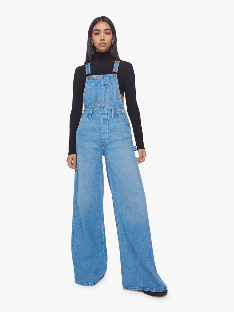 Front view of a woman mid-blue wide leg overalls feature a loose, full leg, a hammer loop and a 32-inch inseam. 