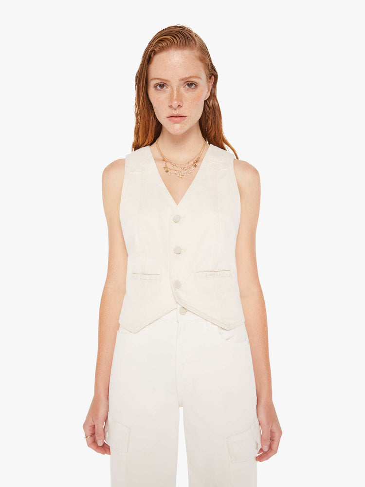 Front view of a woman wearing an off white denim vest featuring three tonal buttons and two front welt pockets.
