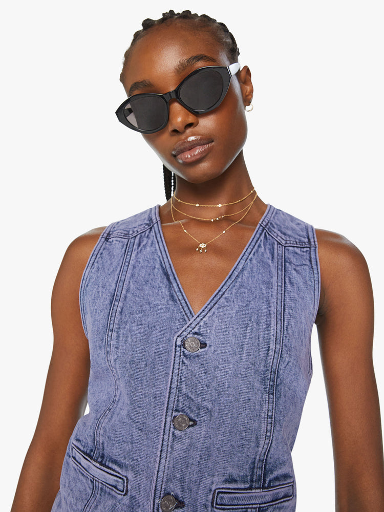 Close up view of a woman denim vest with a V-neck, front seams, slit pockets, an angled hem and a narrow fit in a purple hue.