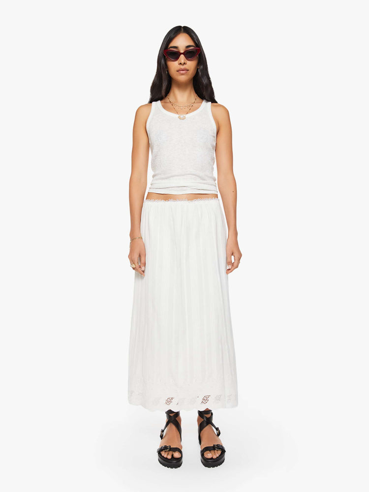 Front view of a woman in a white vintage-inspired midi skirt with a mid-rise, loose, boxy fit, and eyelet-embroidered lace trim. 