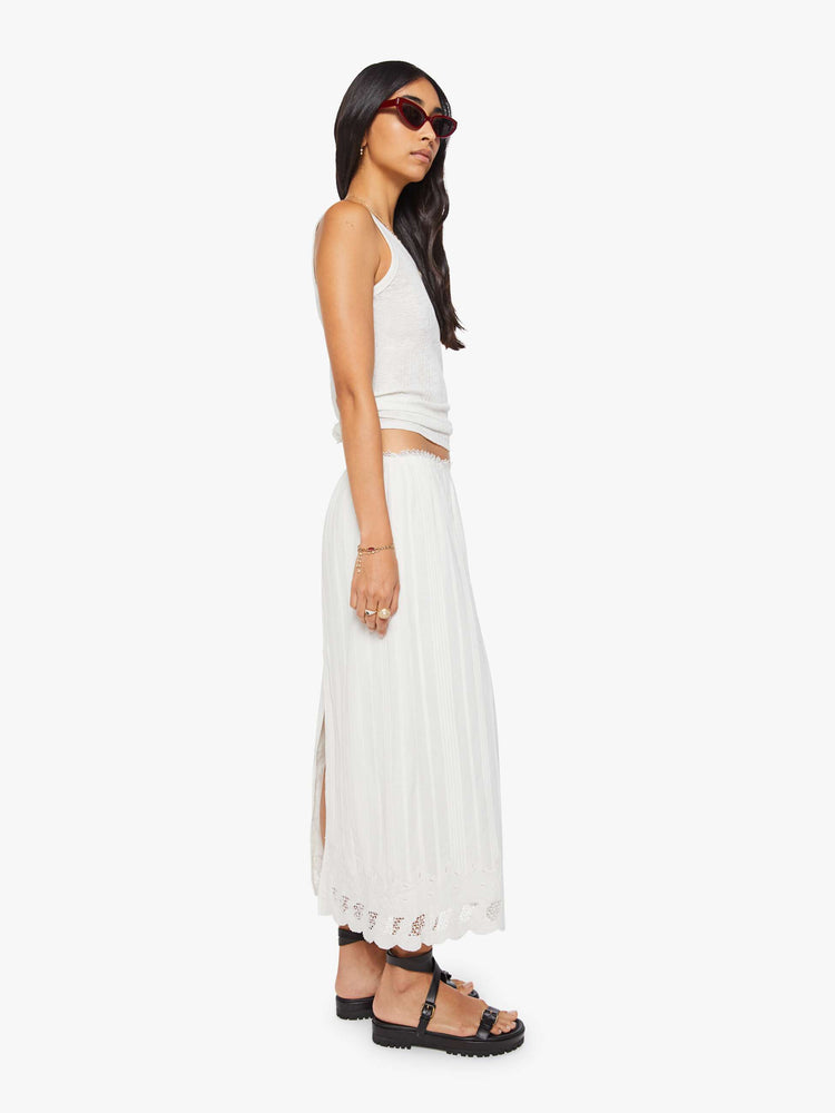 Side view of a woman in a white vintage-inspired midi skirt with a mid-rise, loose, boxy fit, and eyelet-embroidered lace trim. 