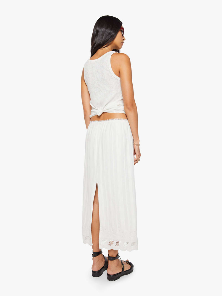 Back view of a woman in a white vintage-inspired midi skirt with a mid-rise, loose, boxy fit, and eyelet-embroidered lace trim. 