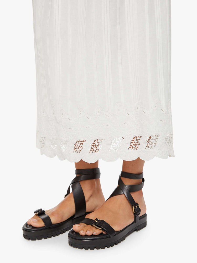 Hem close up view of a woman in a white vintage-inspired midi skirt with a mid-rise, loose, boxy fit, and eyelet-embroidered lace trim. 