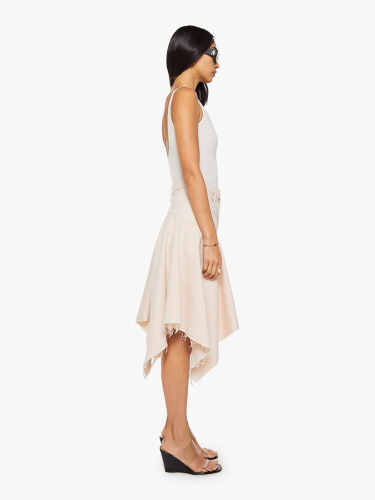 Side view of a woman in pure peach high-waisted midi skirt that's fitted at the hips with a zip fly, flowy, gathered skirt and an uneven, frayed hem.