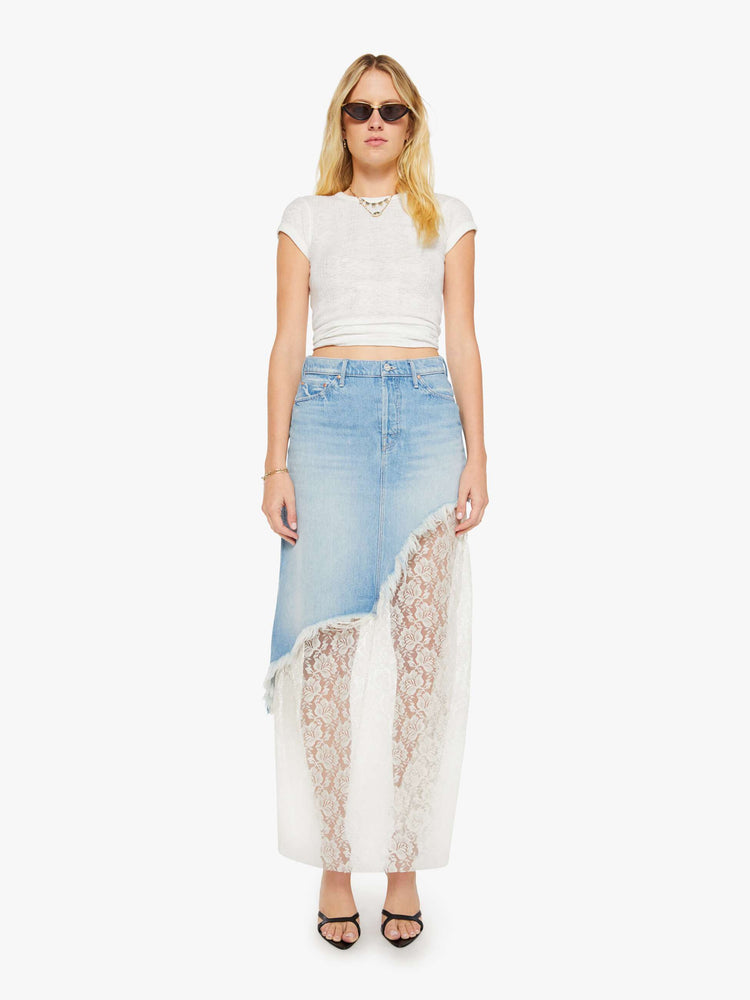 Front view of a woman in a light blue denim maxi skirt with a high rise, button fly, angled frayed hem and sheer lace slip underneath that hits at the ankles. 
