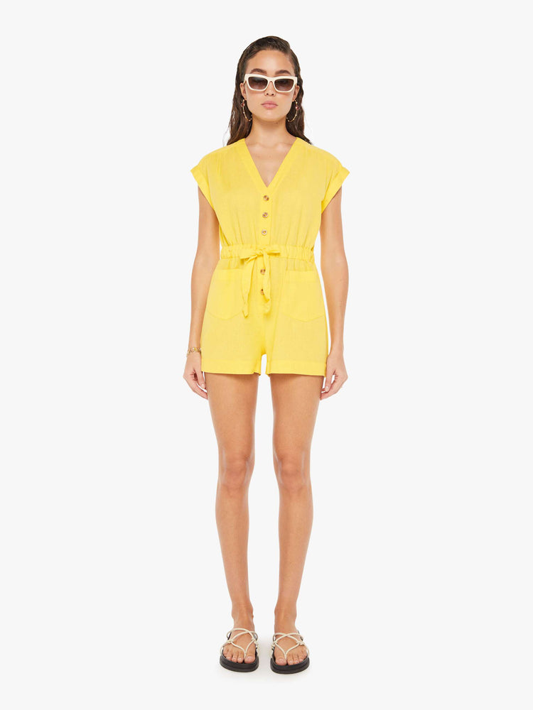 Front view of a woman wearing a short yellow romper featuring cuffed cap sleeves, a v neckline, and an elastic tie waist.