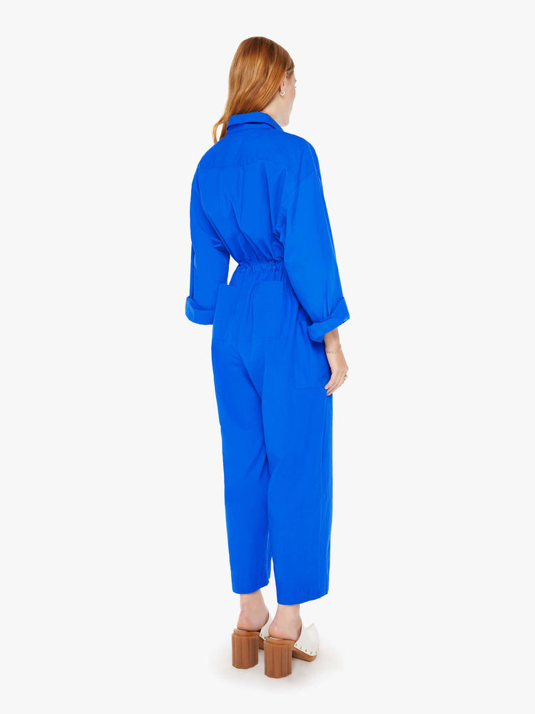 Back view of a woman royal blue lightweight collared jumpsuit with longsleeves, a tied waist, cargo patch pockets and an ankle-length straight leg.